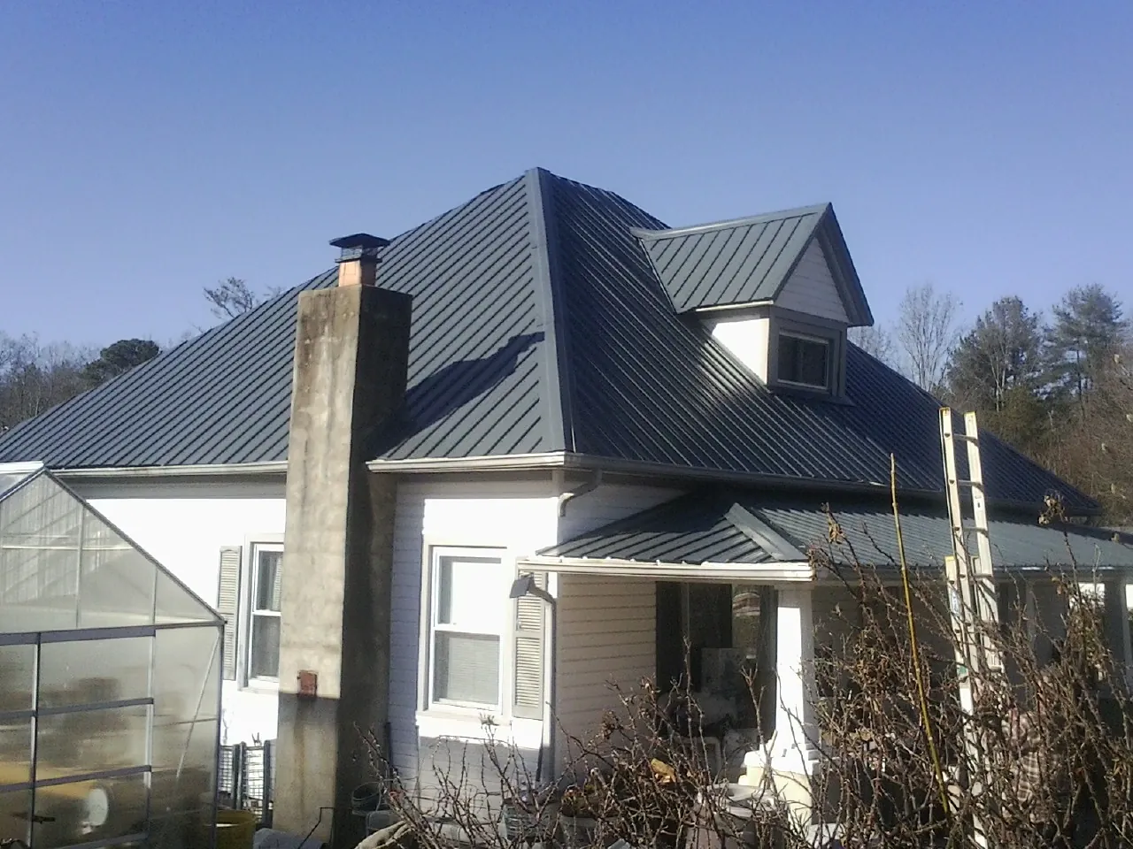 Dark blue standing seam metal roof on a white farmhouse with dormer — Slate & Tile Roof Repair by Roofing Brothers in Woodmere