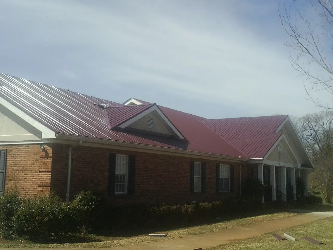 Red metal roof with gabled entries on a long brick building, from a Hail Damage Roof Repair job in Woodmere