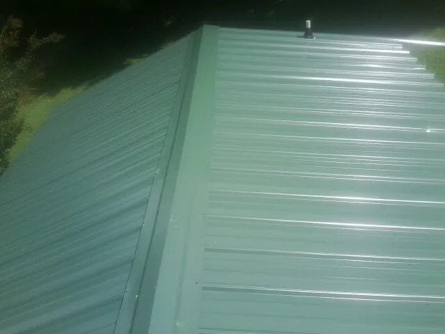 New green metal panels meeting at the ridge of a roof — Flat Roof Repair work by our crew in Woodmere