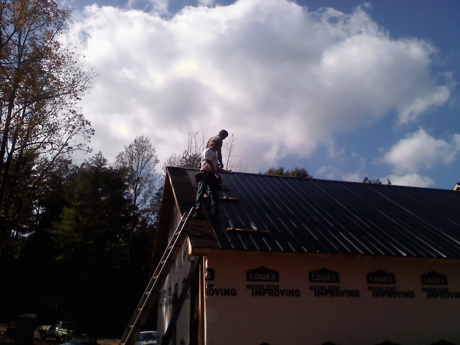 Roofer fastening dark metal panels high against a cloudy sky, from a Roof Inspection job in Woodmere