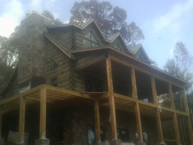 Stone chimney and dormers on a large log home with a timber porch in Woodmere