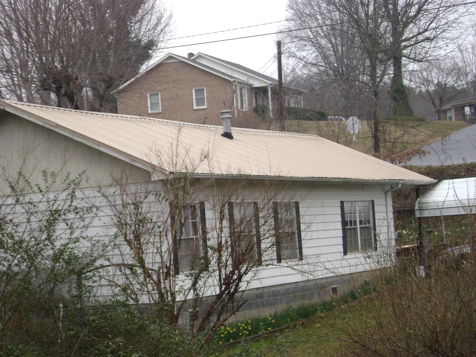 Tan metal roof on a white sided house set into a hillside — Commercial Roofing by Roofing Brothers in Woodmere