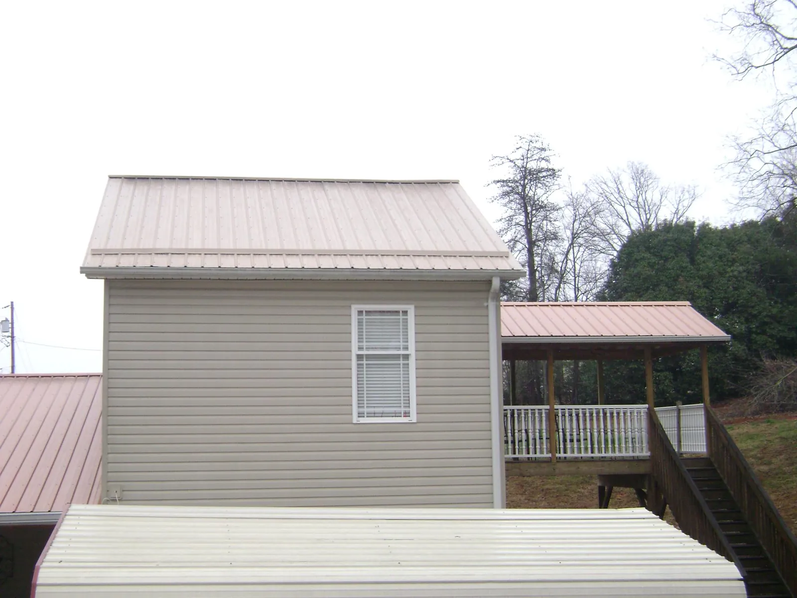 Tan metal roofs on a two story addition and attached porch, from a Roof Replacement job in Woodmere