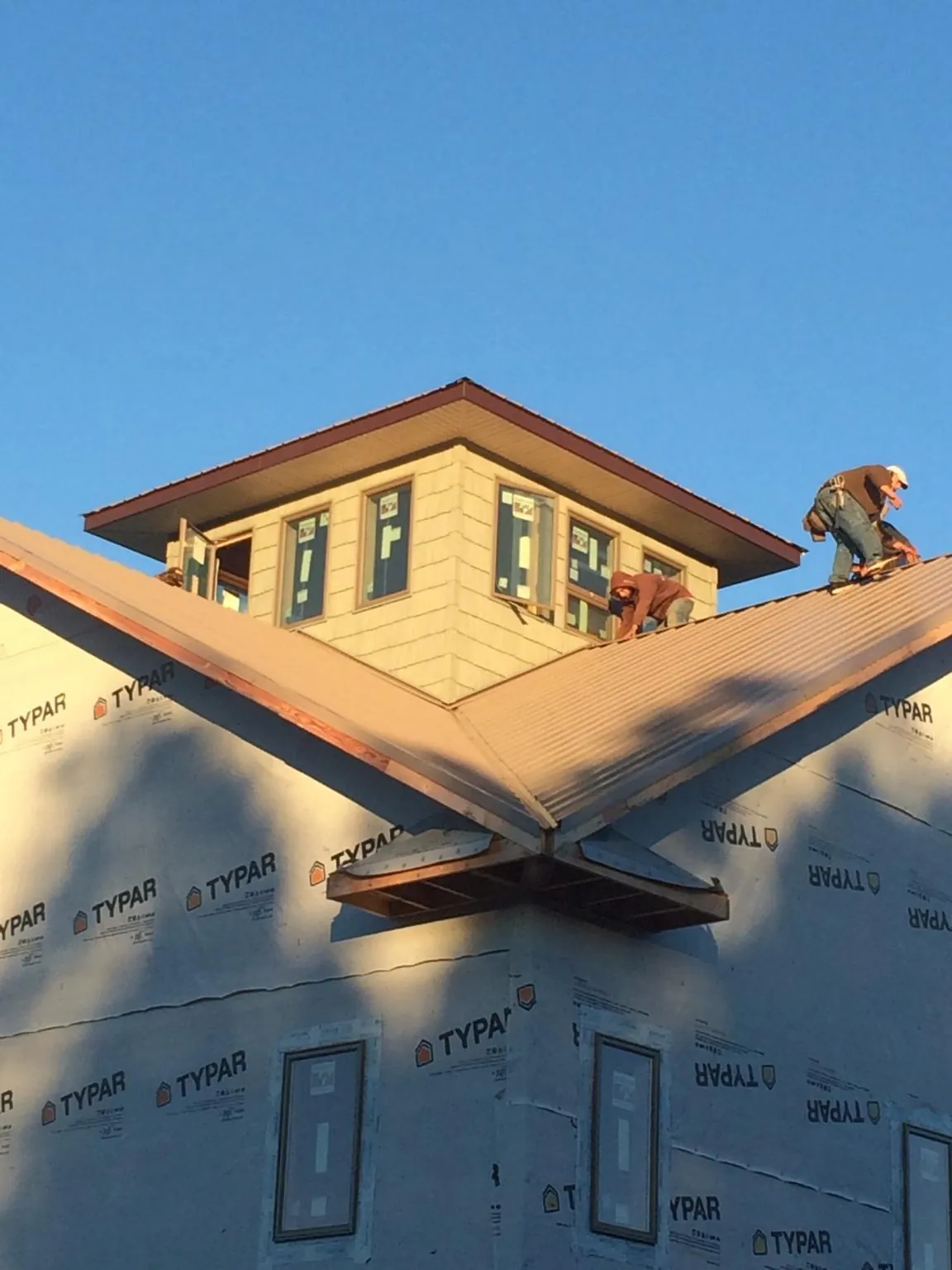 Roofers working around a rooftop cupola on a new metal roof at sunset — Roof Waterproofing in Woodmere by Roofing Brothers